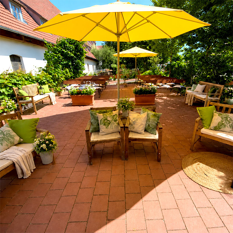 Terrasse mit gelben Sonnenschirmen, Holzbänken, grünen Kissen und Pflanzen für Familienfeste im Freien